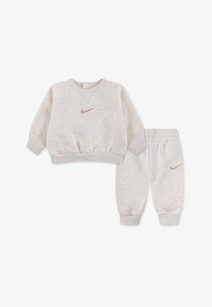 Šviesiai pilkas, minkštas medvilninis džemperis su apvalia iškirpte, gofruotomis rankogaliais ir auksiniu Nike logotipu; derančios sportinės kelnės su elastine juosmens dalimi ir rankogaliais.