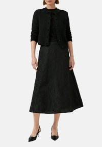 Cardigan noir avec encolure ronde, tissu texturé et fermeture à boutons, associé à une jupe noire longueur cheville avec un motif floral.