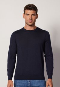 Navy blue crew neck sweater, made of soft fabric, featuring long sleeves and ribbed cuffs, worn with light blue denim jeans.