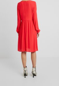 Robe rouge à manches longues avec une taille cintrée et une jupe évasée. Elle présente un dos ajouré et est associée à des bottines imprimé serpent.