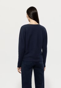 Dunkelblauer Pullover mit rundem Halsausschnitt, langen Ärmeln, leicht strukturiertem Stoff und lässiger Passform, kombiniert mit passenden dunklen Hosen.