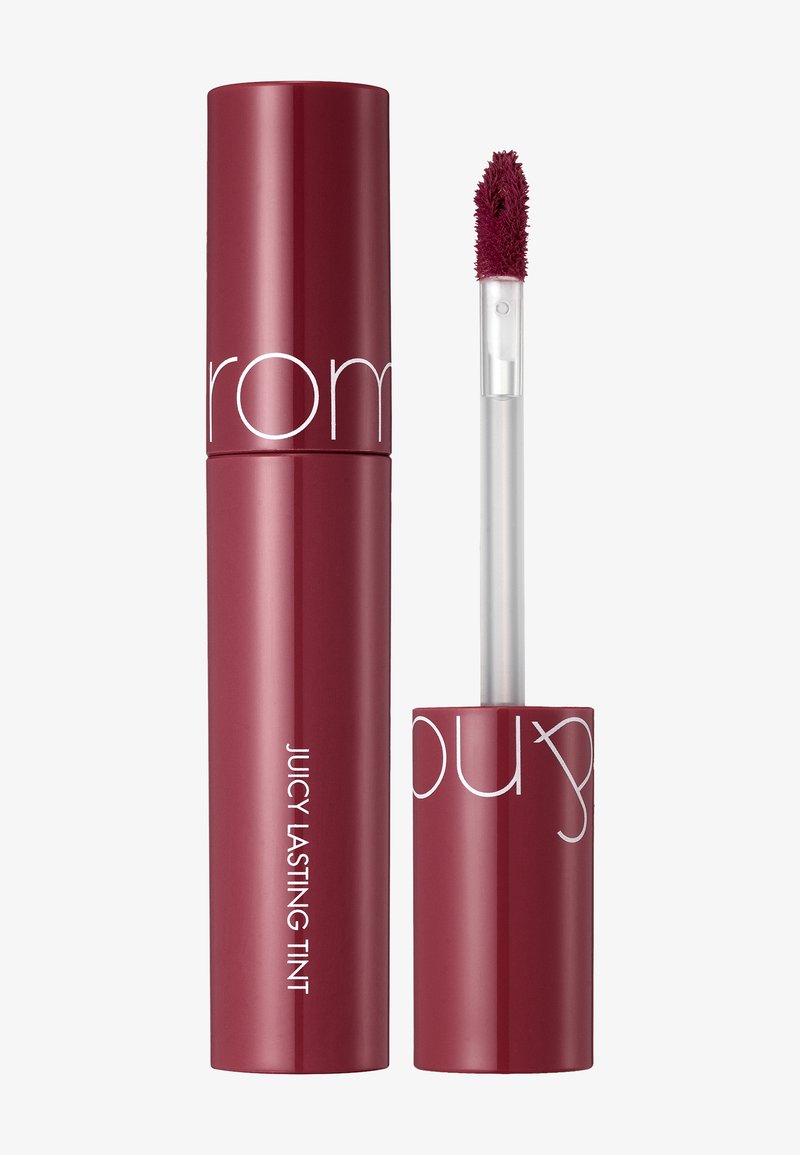 Czerwona tubka o błyszczącym wykończeniu z etykietą "Juicy Lasting Tint." Zawiera przezroczystą aplikatorową różdżkę z miękkim, puszystym końcem.