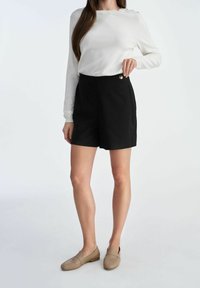 Biała bluzka z długim rękawem i guzikami w połączeniu z czarnymi spodniami typu tailor. Beżowe buty wsuwane dopełniają outfit.