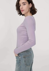 Lichtpaars shirt met lange mouwen en een aansluitend ontwerp, gemaakt van een zachte stof. Gecombineerd met hoog-was denim jeans in een middelmatige kleur.