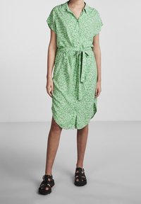 Grön blommig klänning med korta ärmar, knappslå framtill, midjeband och rundad fåll. Kombinerad med svarta sandaler med remmar.