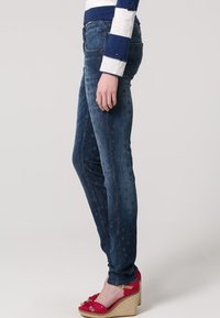 Smal jeans i mörkblå denim med ett stjärnmönster. Bärs med röda kilklackssandaler. Skjortan har marinblå och vita ränder med knappdetalj.