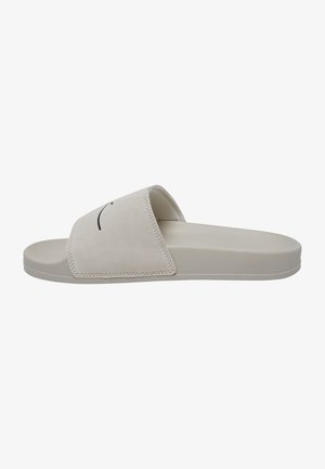 Beige nubukist valmistatud sussid laia rihmaga, tekstuuriga pinnaga ja siledast kummist tallaga. Minimalistlik disain, millel on peened õmblusdetailid.