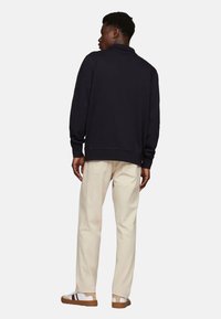 Sudadera azul marino con un cuello alto, mangas largas y puños acanalados, combinada con pantalones de color beige claro y zapatillas marrones con acentos blancos.