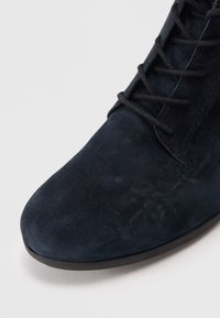 Bottine en suède bleu marine foncé avec un bout rond, des lacets noirs en contraste et une semelle plate en caoutchouc. Texture lisse avec un minimum de coutures.