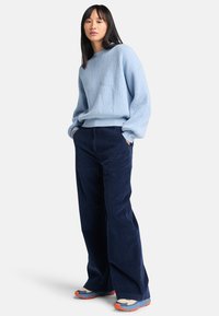 Maglione a coste blu chiaro, pantaloni a gamba larga in corduroy blu navy e sneaker multicolori. L'outfit presenta uno stile casual con una vestibilità rilassata.