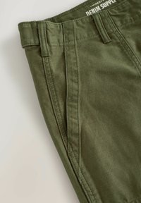 Pantalons vert olive en mélange de coton doux, avec une taille plate, des passants de ceinture et des coutures détaillées le long des côtés.