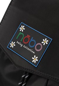 Schwarzer Nylon-Rucksack mit einem rechteckigen Logo, das bunten Text und florale Akzente auf einer strukturierten Oberfläche zeigt.