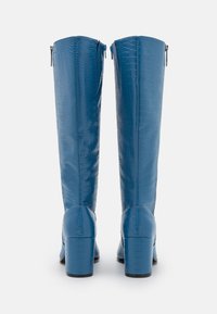 Bottes bleu marine montant jusqu'aux genoux, en cuir embossé crocodile, dotées d'un talon bloc et d'une fermeture éclair à l'arrière pour un enfilage facile. Texture lisse sur toute la surface.