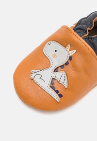 Oranges Leder-Schuh mit strukturierter Oberfläche, der ein graues Drachenmotiv mit blauen Akzenten und einer gestickten Umrandung aufweist. Weicher elastischer Kragen.