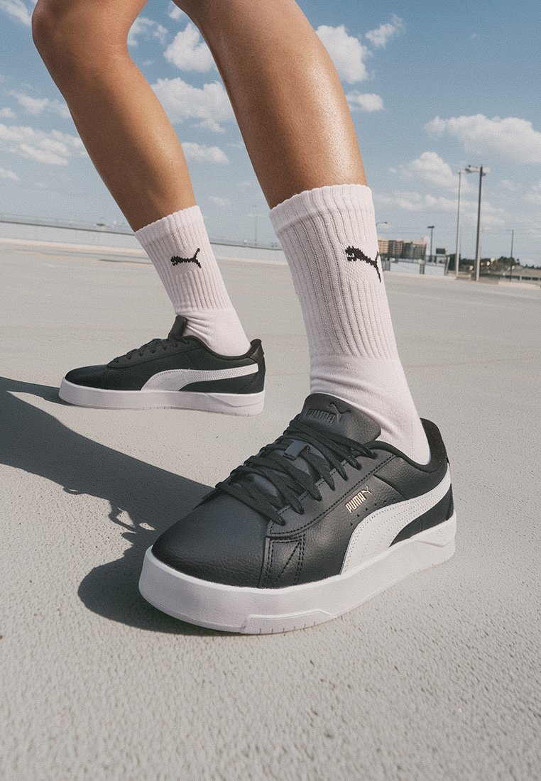 Baskets en cuir noir avec des accents blancs, tige texturée, semelle plate et logo de la marque. Associées à des chaussettes blanches côtelées avec un logo.