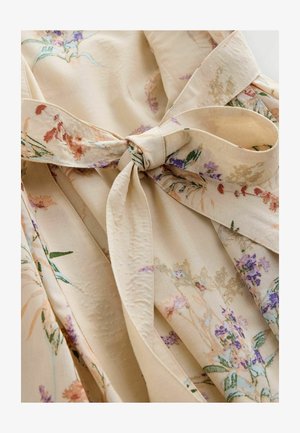 Tissu beige à motif floral avec une texture légère et fluide. Présente une ceinture nouée à la taille et de doux motifs floraux aux couleurs pastel.