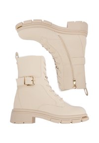 Beżowe skórzane buty wojskowe z sznurowanym przodem, bocznym zamkiem błyskawicznym, detalem klamry, grubą podeszwą i gładką teksturą. Złote akcenty na metalowych elementach.