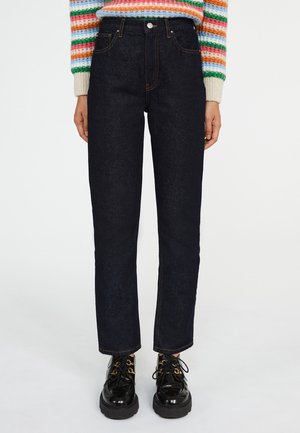 Person iført højtaljede mørkeblå jeans med lige ben, farverig stribet sweater og skinnende sorte snørestøvler med plateau.