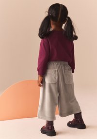Graue Corduroy-Hosen mit weitem Bein und seitlichen Taschen, kombiniert mit einem burgunderfarbenen Langarmshirt und glänzenden burgunderfarbenen Ankle Boots.