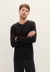 Zwarte V-hals trui met lange mouwen, geribbelde boorden en zoom, gemaakt van zachte stof. Minimalistisch design met een subtiel logo op de borst.