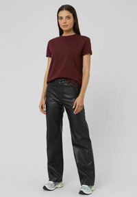 T-shirt bourgogne à col rond avec des manches roulées, associé à un pantalon en faux cuir noir taille haute et des baskets de sport argentées.