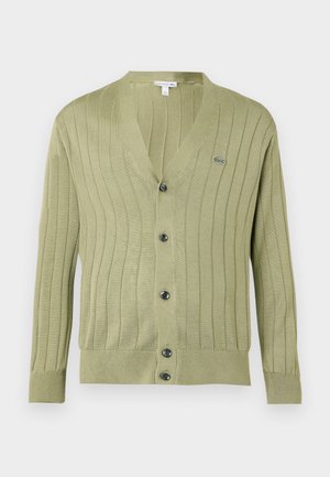 Gilet côtelé d'un vert olive clair avec des manches longues, un col en V, cinq boutons noirs, et un petit logo de crocodile brodé sur la poitrine.