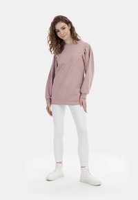 Felpa rosa con maniche a sbuffo, scollo rotondo, polsini e fondo a costine. Abbinata a jeans skinny bianchi e sneakers alte bianche.