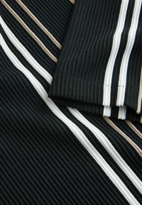 Tissu noir côtelé avec des rayures verticales blanches et beige, montrant une manche pliée avec un motif rayé assorti.