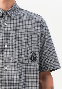 Short-sleeve, checkered shirt in navy and white fabric; features a left chest pocket with a black embroidered serpent design.