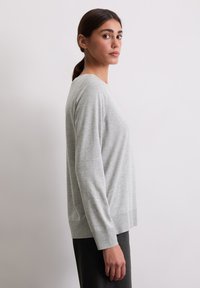 Hellgraues Langarmshirt aus weichem Stoff, mit Rundhalsausschnitt und lockerer Passform, vor einem schlichten Hintergrund präsentiert.