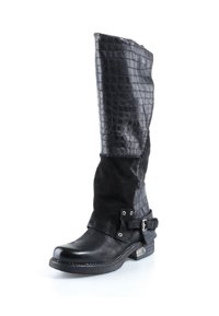 Botte haute en cuir noir avec partie supérieure texturée, partie inférieure lisse, sangle à boucle près de la cheville et talon bas empilé sur fond blanc.