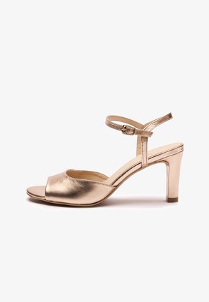 Sandalia de tacón alto en rosa dorado metálico con correa al tobillo y hebilla, punta abierta y tacón ancho de altura media sobre fondo blanco.