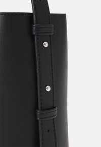 Černá kožená taška přes rameno s hladkou texturou, vybavená prošitým popruhem upevněným stříbrnými nýty a minimalistickým designem.