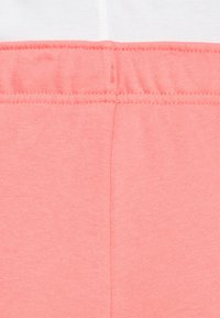 Koraalroze sweatpants van een zachte, textuurachtige stof. Voorzien van een elastische tailleband en eenvoudige stiksels langs de naad. Geen opvallende patronen.