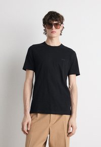 Čierne tričko s krátkym rukávom vyrobené z bavlny, s okrúhlym výstrihom a jemným logom "BOSS" na prednej strane, v kombinácii s béžovými nohavicami.