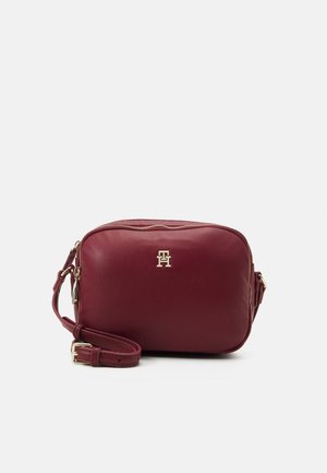 Compact burgundy leather crossbody bag with adjustable strap and gold-tone logo and zipper detailing on a plain background.
