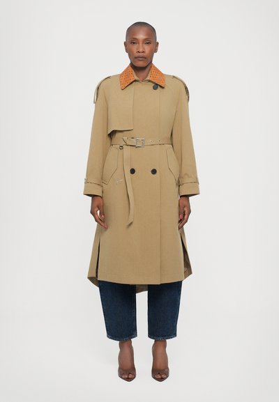 Beige Trenchcoat mit einem texturierten orangen Kragen, doppelt geknöpftem Frontverschluss und Gürtel. Kombiniert mit lockeren, dunklen Jeans und braunen High Heels.