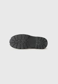 Black rubber shoe sole with a rugged design featuring deep treads and grooves for traction, flat profile, and a smooth surface area.