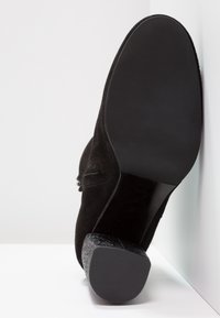 Czarne zamszowe botki do kostki z gładkim, okrągłym czubkiem i teksturowanym obcasem. Podeszwa jest płaska i prosta, o czarnym wykończeniu.