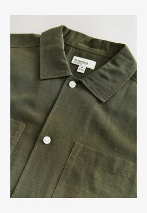 Õlivihjeroheline särk kraega, kahe eesmise tasku ja valgete nööpidega. Valmistatud tekstuurse kangaga, millel horisontaalsed triibud.