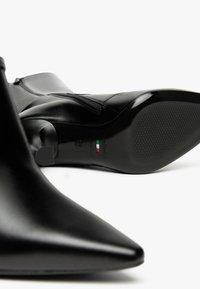 Stivaletti neri con punta a punta realizzati in pelle liscia. Presentano una chiusura con zip, una suola testurizzata e un branding discreto sul tallone.