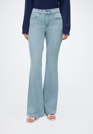 Jeans a vita alta e gamba svasata azzurri chiaro indossati con una maglia a maniche lunghe blu navy e sandali bianchi con tacco e punta aperta.