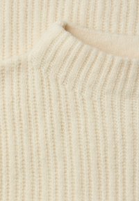 Kremowy, dzianinowy materiał swetra o pionowej prążkowanej fakturze i wysokim dekolcie, wykonany z miękkiego, przytulnego materiału z czystym wykończeniem.