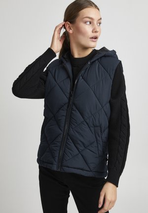Gilet matelassé bleu marine avec capuche, doté d'une fermeture éclair frontale, de poches latérales et de manches tricotées noires texturées avec un motif en câble.