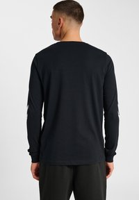 Schwarzes Langarmshirt aus Baumwolle. Hat einen Rundhalsausschnitt und weiße Akzentdesigns an jedem Ärmel. Glatte Textur, lässige Passform.