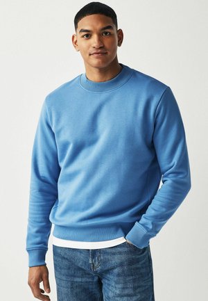 Blå crew-neck sweatshirt lavet af blød bomuldsblanding, med ribbede cuff og talje, parret med lyse denimjeans.