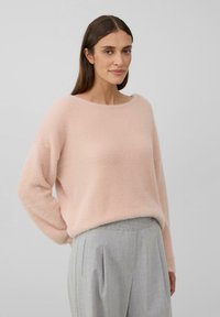 Pull en maille rose clair et moelleux, avec un décolleté large et des manches longues, associé à un pantalon cintré gris clair avec un design plissé.