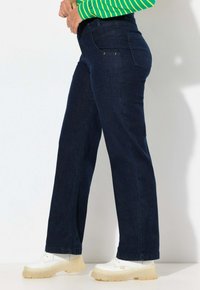 Vaqueros de mezclilla de color azul oscuro con corte recto, cinco bolsillos y acentos de costura mínimos. Combinados con zapatillas de plataforma blancas.