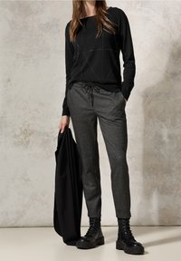 Svart tröja med geometriska metalliska detaljer, tillsammans med grå sweatpants med houndstooth-mönster och svarta snörstövlar.