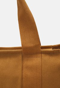 Bolsa de tote de algodón en color amarillo mostaza con una superficie texturada y asas trenzadas resistentes. El cuerpo principal presenta un sencillo pespunte a lo largo de los bordes.